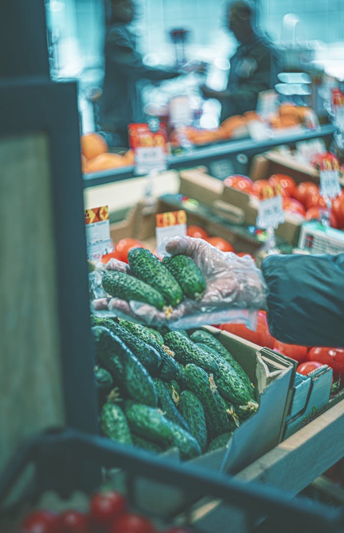 Man choosing fresh cucumbers at a bustling farmers market indoors.